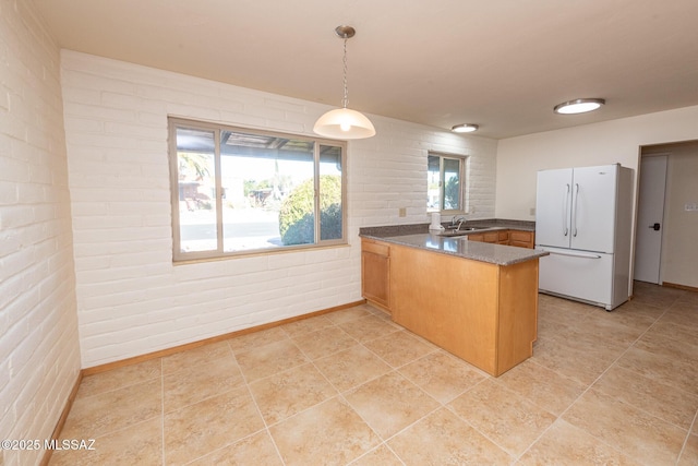 kitchen with white refrigerator, sink, decorative light fixtures, kitchen peninsula, and brick wall