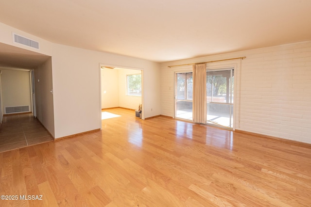 unfurnished room featuring a healthy amount of sunlight, brick wall, and light hardwood / wood-style flooring