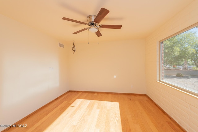 unfurnished room with hardwood / wood-style floors, plenty of natural light, ceiling fan, and brick wall