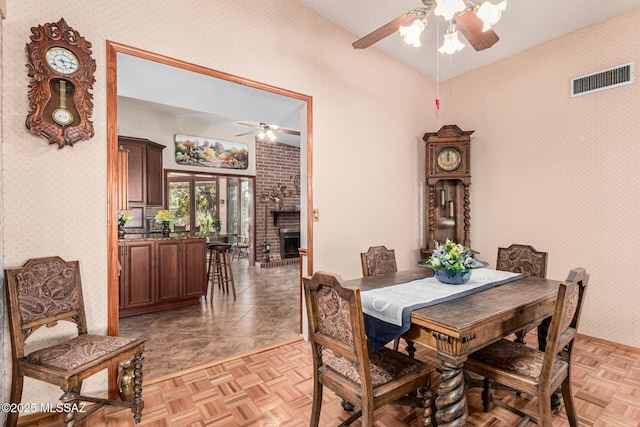 dining space featuring vaulted ceiling, a brick fireplace, light parquet flooring, and ceiling fan