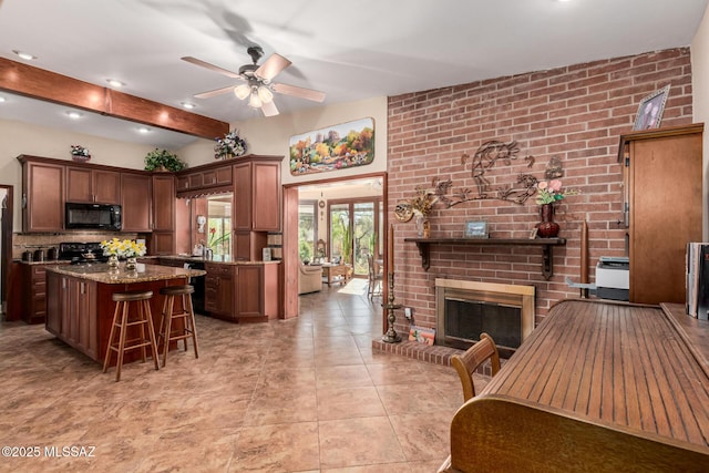 kitchen featuring ceiling fan, range, black microwave, a center island, and light stone counters