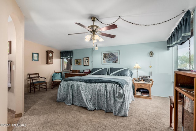 carpeted bedroom with arched walkways, multiple windows, and ceiling fan