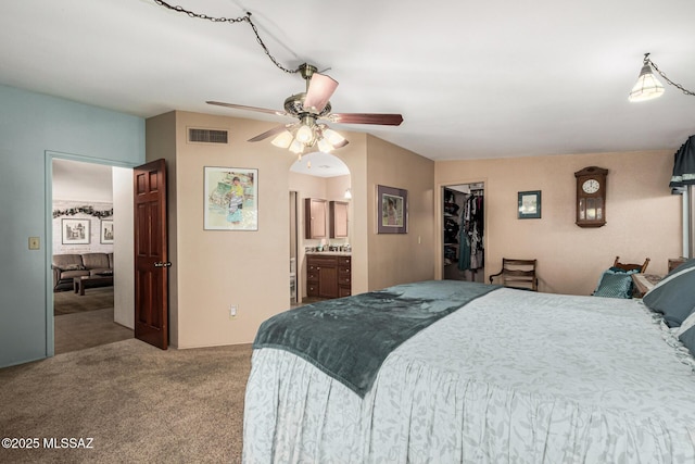 bedroom with a walk in closet, a closet, ceiling fan, light carpet, and ensuite bathroom