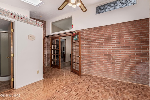 unfurnished room with ceiling fan, a skylight, light parquet flooring, and brick wall