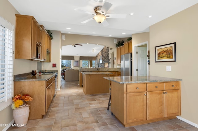 kitchen with a kitchen island, appliances with stainless steel finishes, a breakfast bar area, ceiling fan, and light stone counters