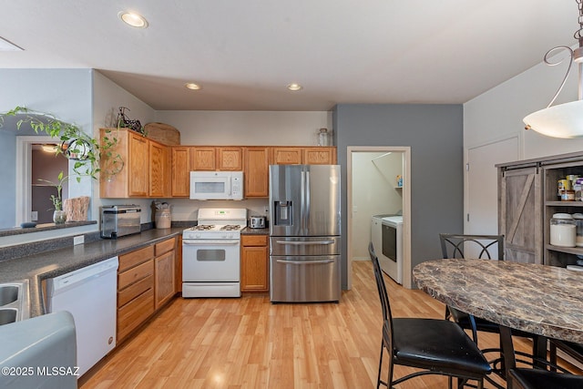 kitchen featuring hanging light fixtures, a barn door, white appliances, washer / dryer, and light wood-type flooring