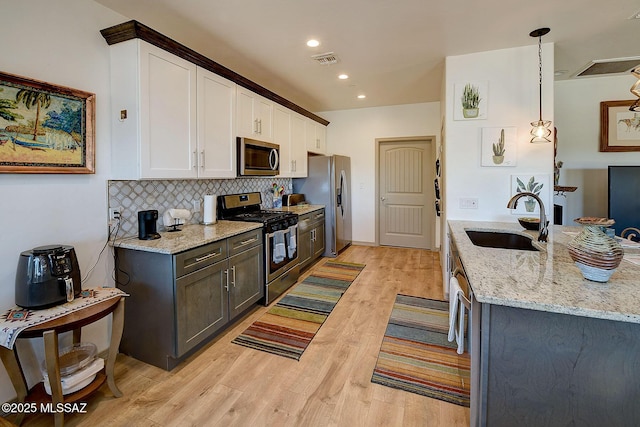 kitchen featuring appliances with stainless steel finishes, decorative light fixtures, light stone countertops, white cabinets, and sink