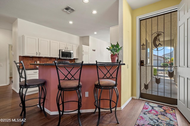 kitchen featuring white cabinetry, dark hardwood / wood-style flooring, backsplash, kitchen peninsula, and a breakfast bar area