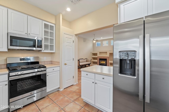 kitchen featuring white cabinets, stainless steel appliances, and a brick fireplace