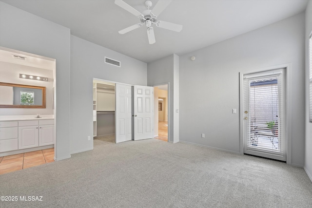 unfurnished bedroom featuring sink, ceiling fan, a spacious closet, connected bathroom, and light colored carpet