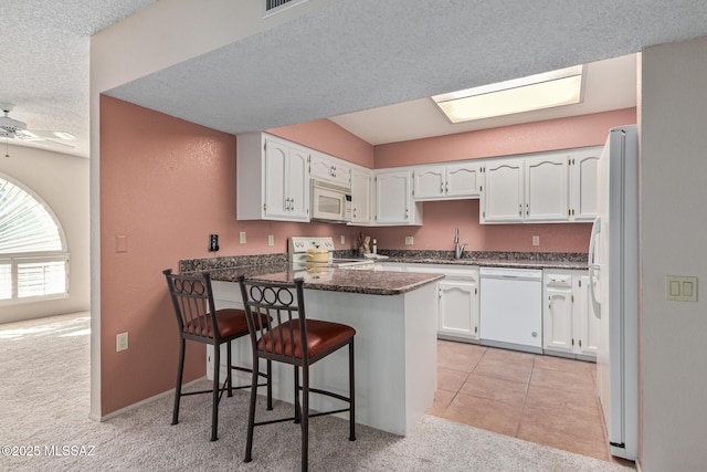 kitchen with white cabinetry, white appliances, light carpet, kitchen peninsula, and a breakfast bar area