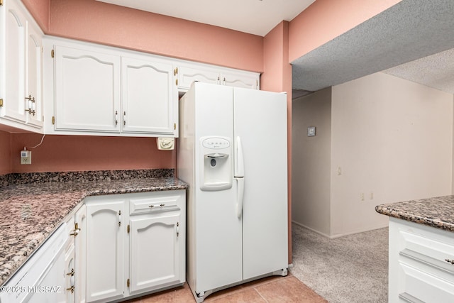 kitchen featuring white cabinetry, a textured ceiling, white fridge with ice dispenser, dark stone counters, and light colored carpet