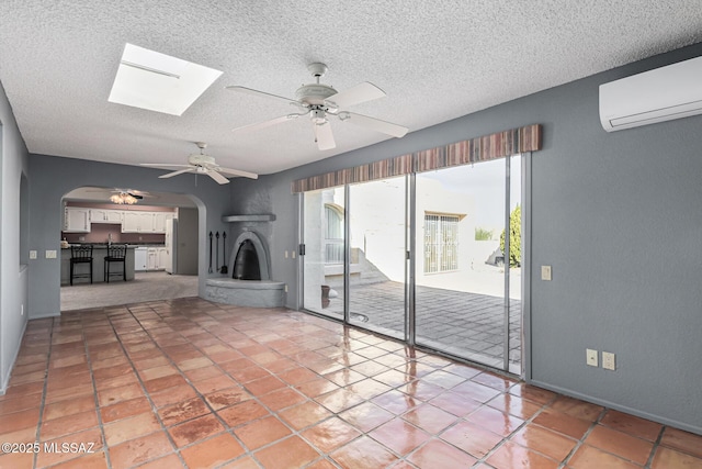 unfurnished living room featuring a textured ceiling, ceiling fan, a skylight, and a wall mounted air conditioner