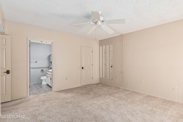 unfurnished bedroom featuring ceiling fan, light colored carpet, ensuite bathroom, and a textured ceiling