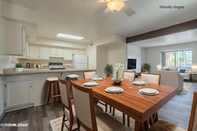 dining room featuring ceiling fan, a skylight, and dark wood-type flooring