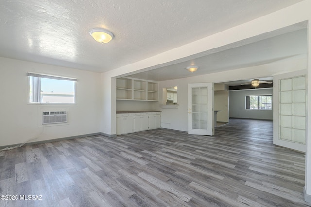 unfurnished living room featuring a healthy amount of sunlight, an AC wall unit, french doors, and a textured ceiling