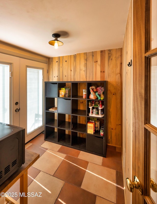 interior space with french doors, light tile patterned floors, plenty of natural light, and wood walls