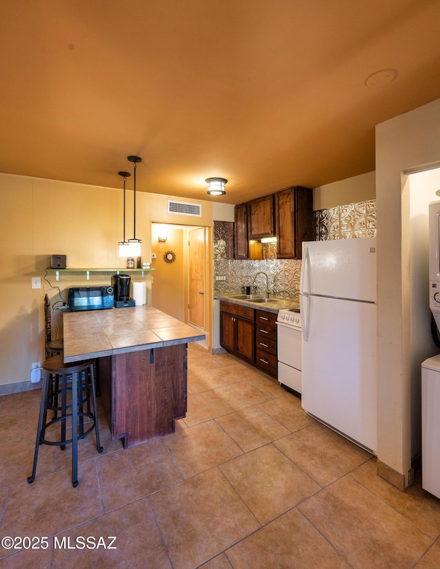 kitchen featuring sink, hanging light fixtures, tasteful backsplash, white appliances, and a kitchen bar