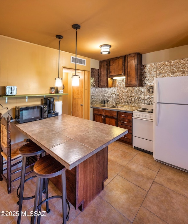 kitchen with a kitchen bar, tasteful backsplash, white appliances, sink, and hanging light fixtures