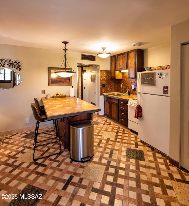 kitchen with sink, tasteful backsplash, pendant lighting, white appliances, and a kitchen bar