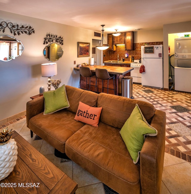 tiled living room with stacked washing maching and dryer and sink