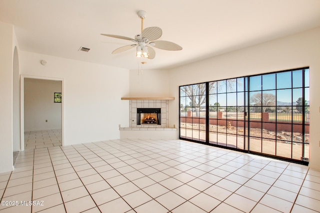 unfurnished living room with a tile fireplace, light tile patterned floors, and ceiling fan