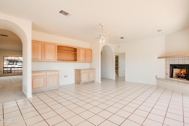 unfurnished living room with ceiling fan, light tile patterned floors, and a tiled fireplace