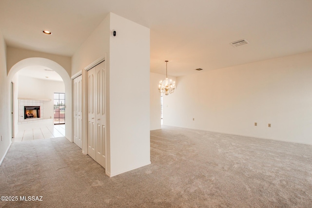 empty room with light carpet, a tile fireplace, and a chandelier