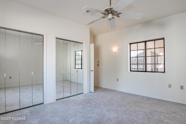 unfurnished bedroom with light carpet, multiple windows, two closets, and ceiling fan