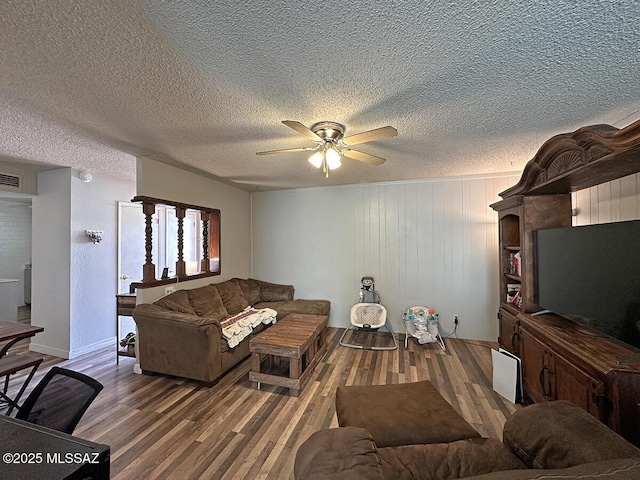 living room featuring a textured ceiling, hardwood / wood-style flooring, ceiling fan, and wooden walls