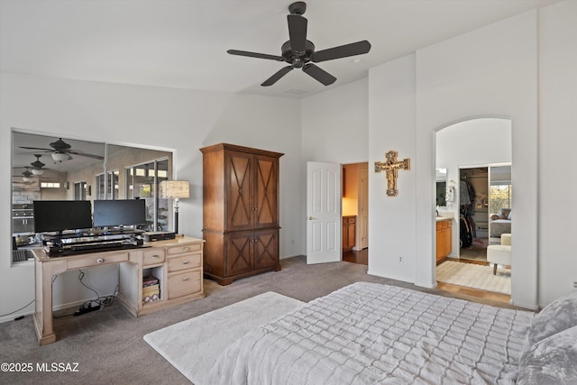 carpeted bedroom with ensuite bath, ceiling fan, and high vaulted ceiling