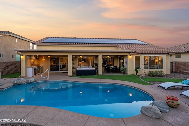 pool at dusk with exterior kitchen, outdoor lounge area, and a patio area