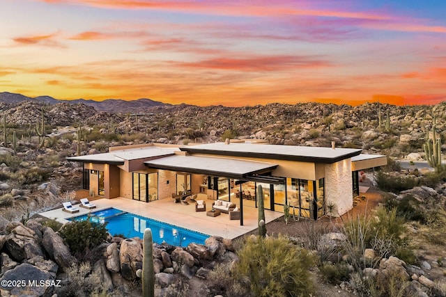 pool at dusk with an outdoor living space, a patio, and a mountain view