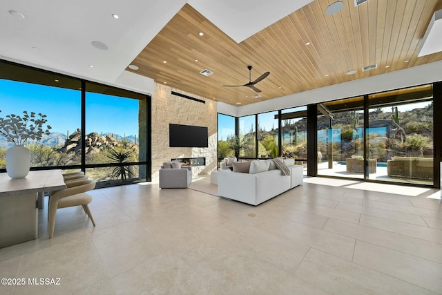 unfurnished living room with a fireplace, wooden ceiling, ceiling fan, and a wall of windows