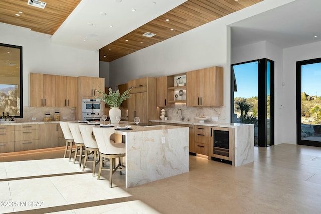 kitchen with beverage cooler, a breakfast bar, a kitchen island with sink, and wooden ceiling