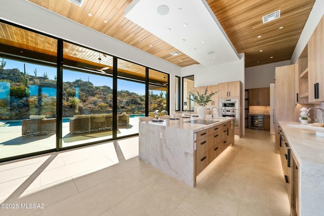 kitchen featuring sink, wood ceiling, light tile patterned floors, a large island with sink, and light stone countertops