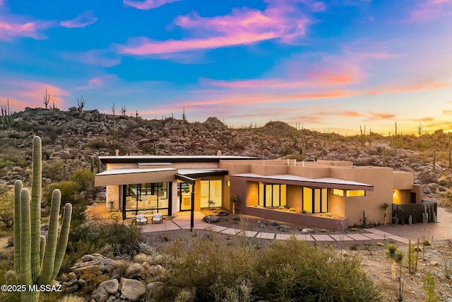 back house at dusk with a fireplace and a patio