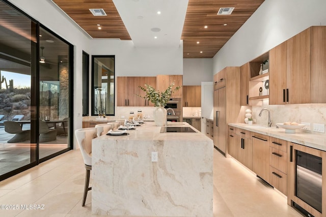 kitchen featuring a kitchen bar, sink, wooden ceiling, beverage cooler, and a large island