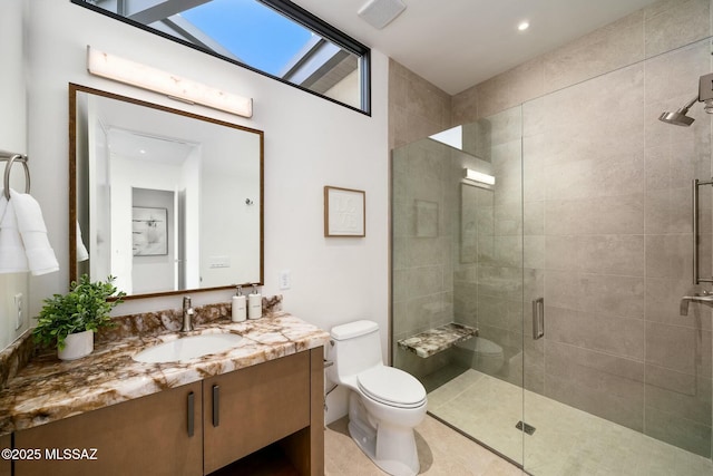 bathroom with a skylight, tile patterned flooring, vanity, walk in shower, and toilet