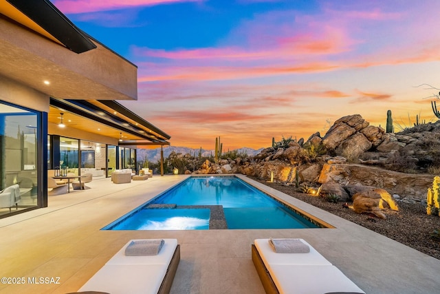 pool at dusk featuring a patio area and an in ground hot tub