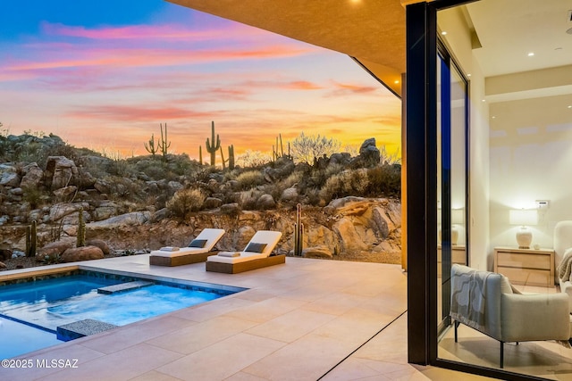 pool at dusk with an in ground hot tub and a patio