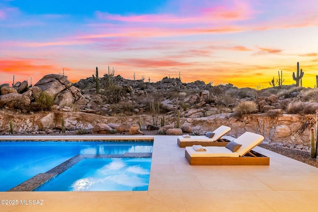 pool at dusk with a patio and an in ground hot tub