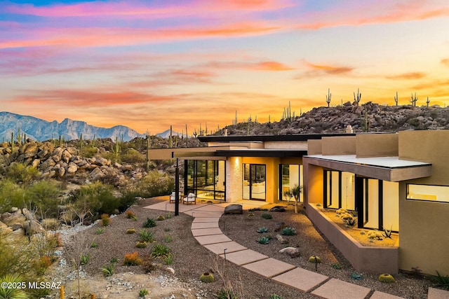 back house at dusk featuring a mountain view and a patio