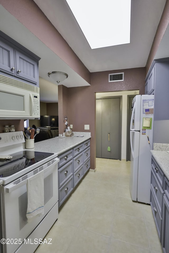 kitchen with white appliances, a skylight, gray cabinets, light stone countertops, and light tile patterned flooring