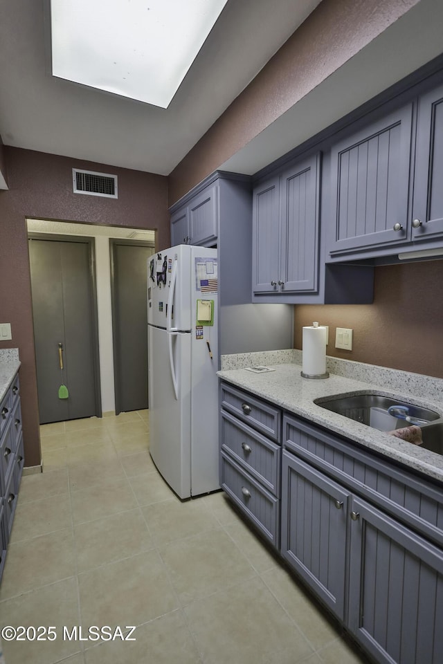 kitchen featuring white refrigerator, gray cabinets, and light stone counters