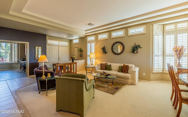 living room featuring a tray ceiling, visible vents, and baseboards