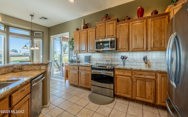 kitchen with appliances with stainless steel finishes, brown cabinets, decorative backsplash, and light tile patterned floors