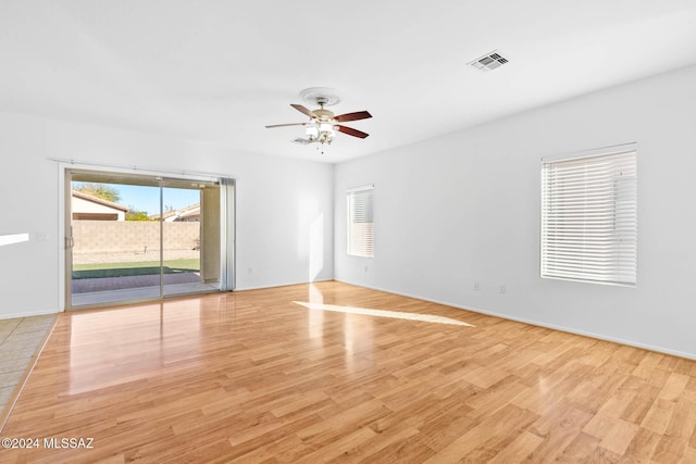 empty room featuring plenty of natural light, ceiling fan, and light wood-type flooring