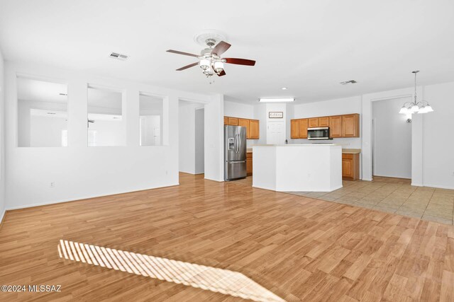 unfurnished living room featuring ceiling fan with notable chandelier and light hardwood / wood-style flooring