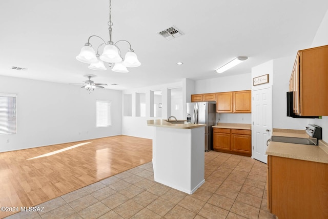 kitchen with stainless steel fridge, ceiling fan with notable chandelier, decorative light fixtures, range, and an island with sink